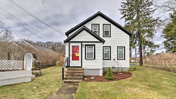 A two-story house with a front porch, a red door, and a small front yard.