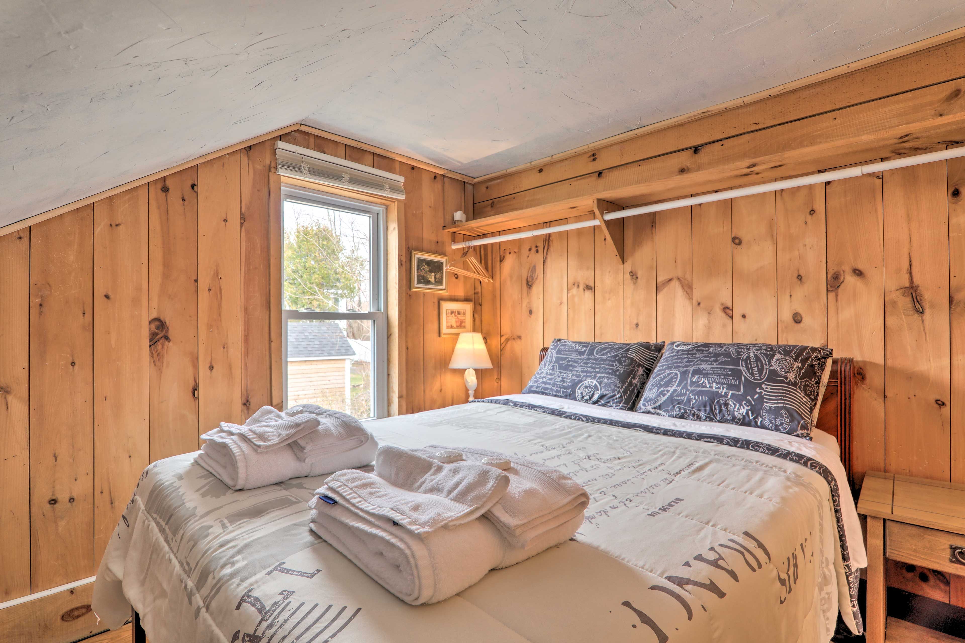 A wooden-paneled bedroom with a bed, towels, a lamp, and a window.