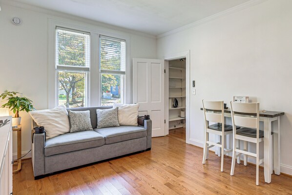 Una habitación con un sofá gris, una mesa de comedor con sillas y una ventana con persianas.