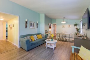 A living room with a sofa, a dining table with chairs, and a kitchen area in the background.