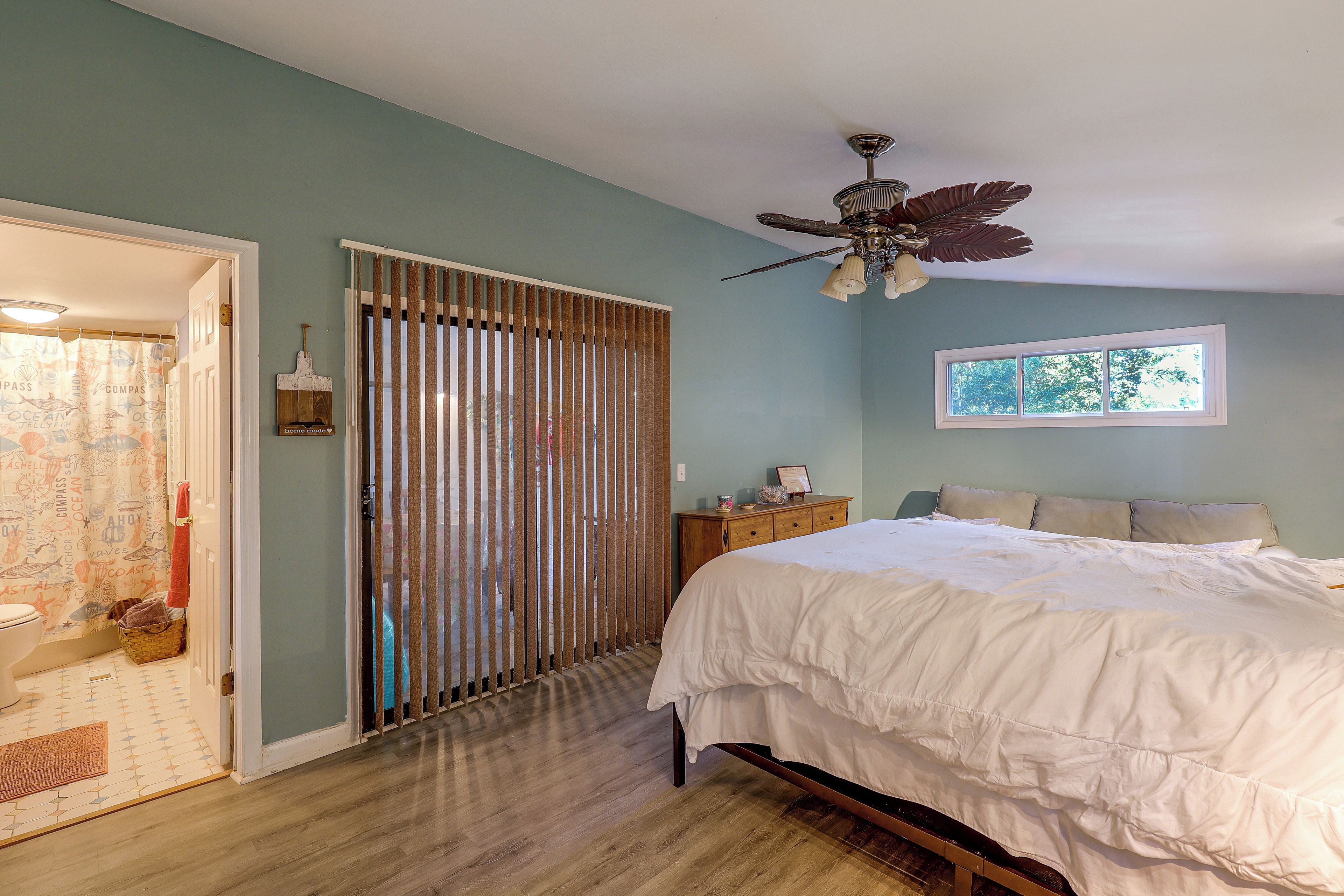 Un dormitorio con cama, ventana, ventilador de techo y una puerta con cortina.