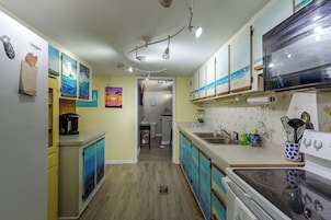 A kitchen with a stove, sink, and cabinets. There is a coffee maker on the counter and a blender. The walls are decorated with artwork.