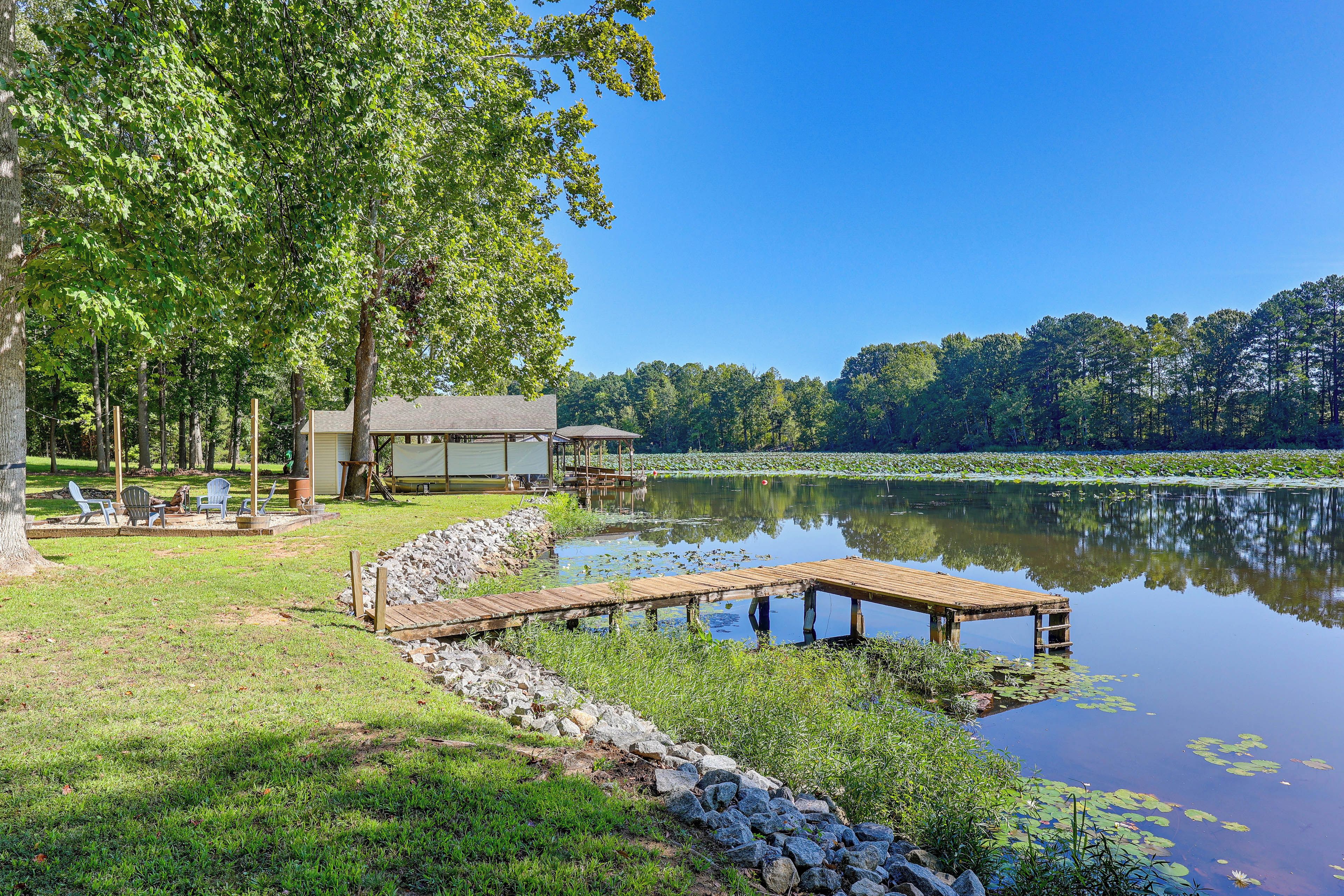 A lakeside property with a dock, outdoor seating, and a building with a covered area.