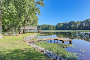 A lakeside property with a dock, outdoor seating, and a building with a covered area.