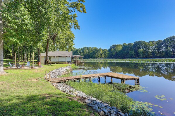 A lakeside property with a dock, outdoor seating, and a building with a covered area.