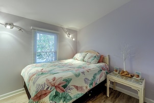 A bedroom with a bed, a nightstand, a window with blinds, and a wall-mounted light fixture.