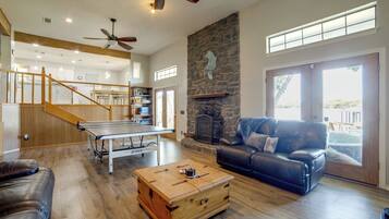 A spacious living area with a ping pong table, leather sofa, and a stone fireplace.