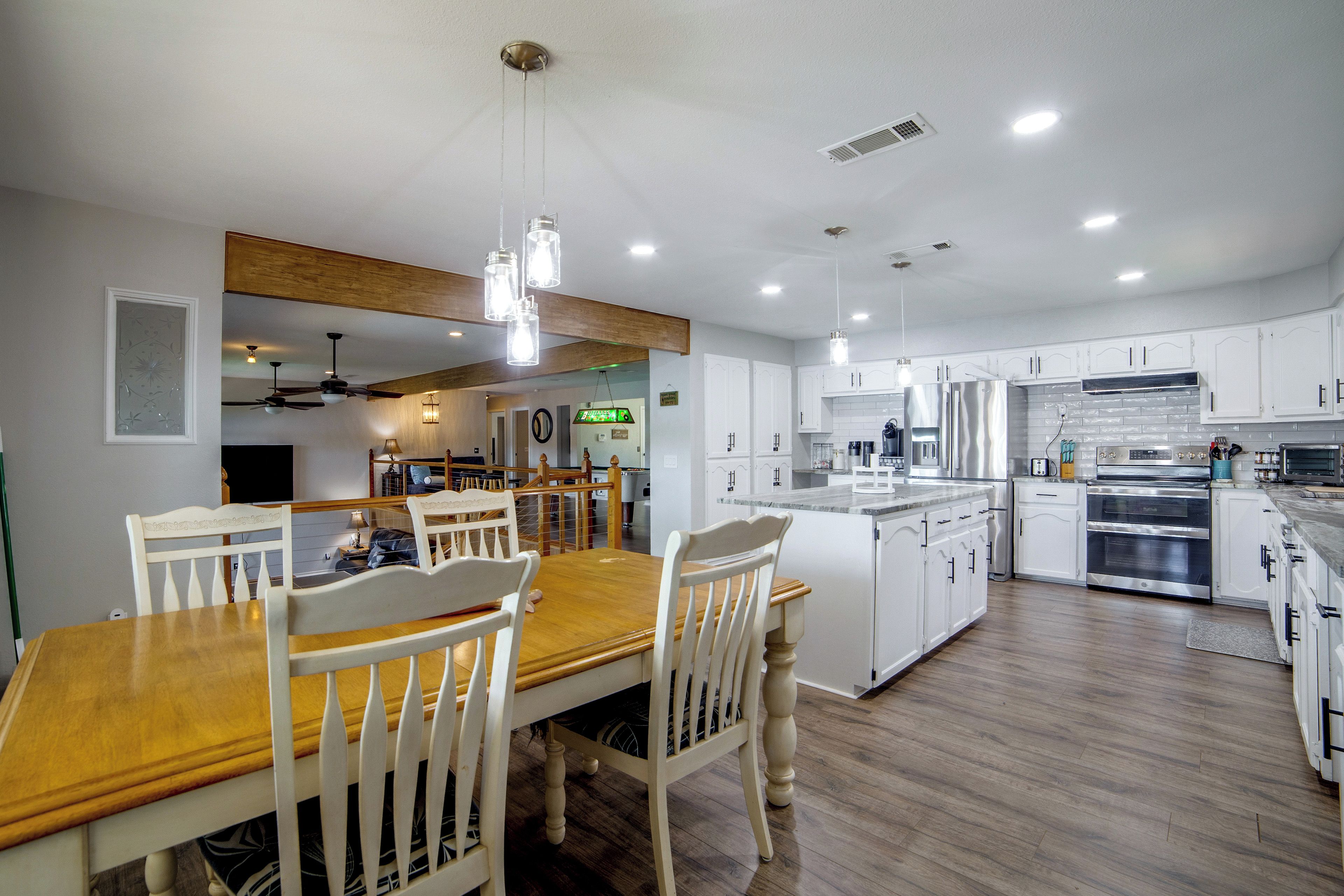 A modern kitchen with white cabinets, stainless steel appliances, and a wooden dining table with chairs.
