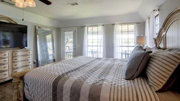 A bedroom with a large bed, a dresser, a television, and a ceiling fan.