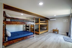A room with two bunk beds, a small wooden table, an air conditioning unit, and a window with curtains.