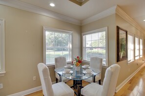 A dining area with a glass table surrounded by white chairs, large windows with blinds, and a hallway with a framed picture on the wall. - 1 Block to Beach! Elegant Family Home in Gulfport (Gulfport)