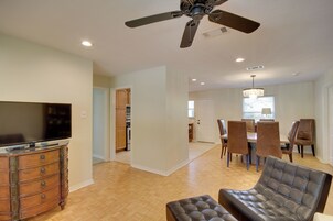 A spacious living room with a flat-screen TV, a leather sofa, and a dining area with wooden chairs.