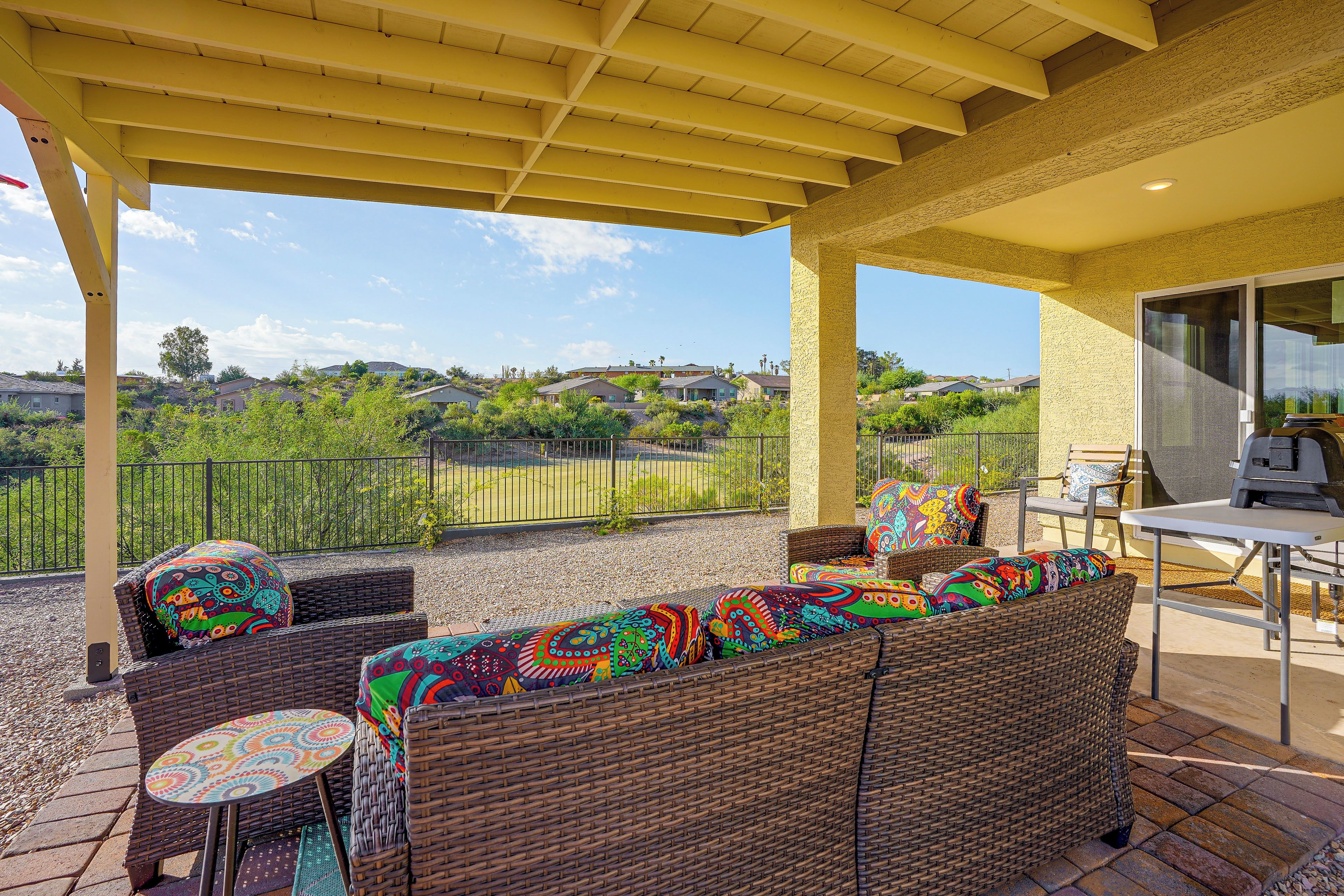 A covered patio with wicker furniture, a table, and a grill.