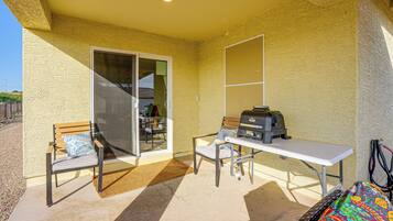 A covered patio area with a table, chairs, a grill, and a bench.