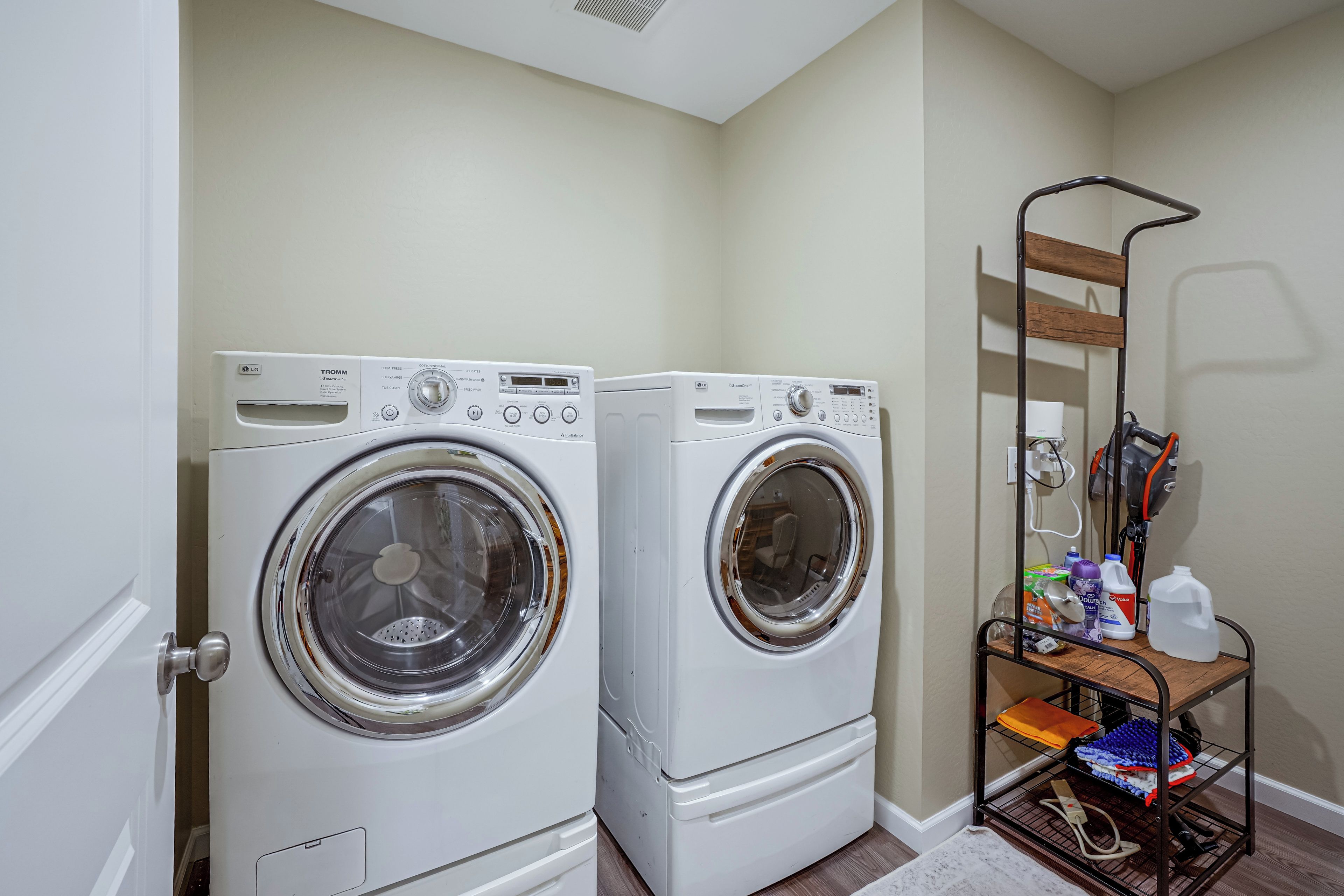 A laundry area with two front-loading washing machines and a metal rack with cleaning supplies.