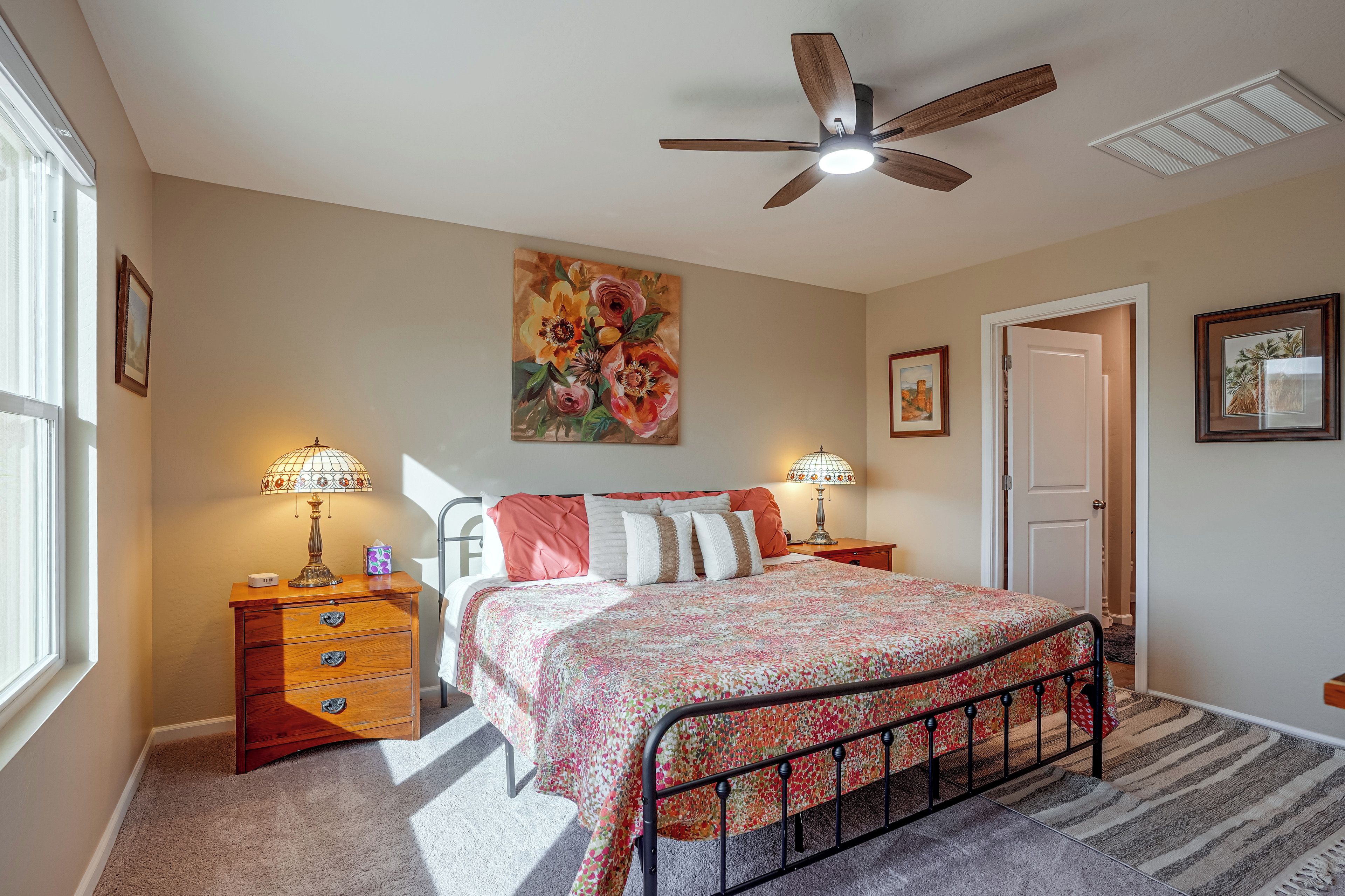 A bedroom with a bed, two nightstands, a ceiling fan, and a painting.