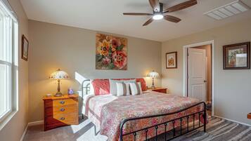 A bedroom with a bed, two nightstands, a ceiling fan, and a painting.