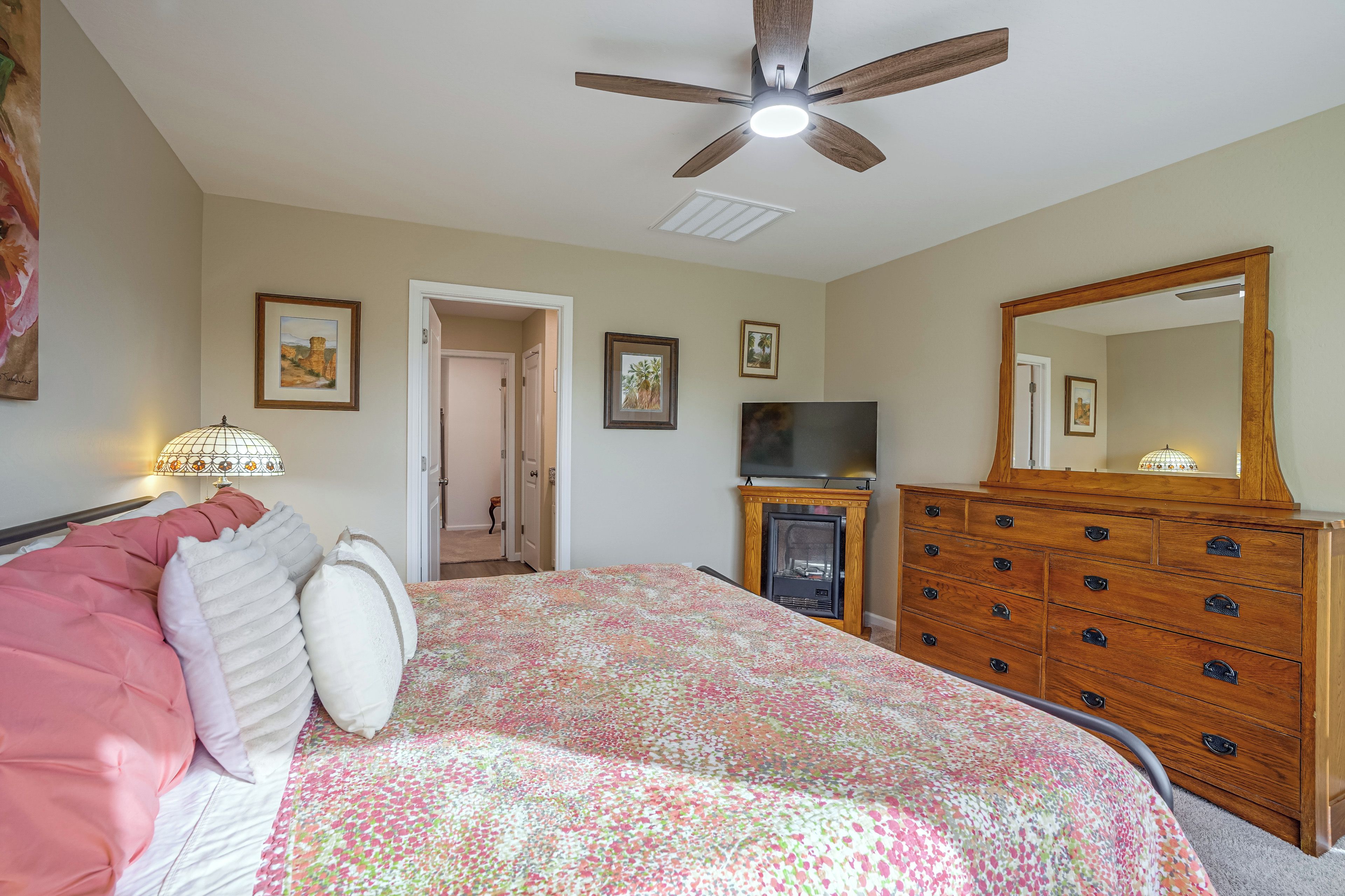 A bedroom with a bed, a dresser, a television, and a ceiling fan.