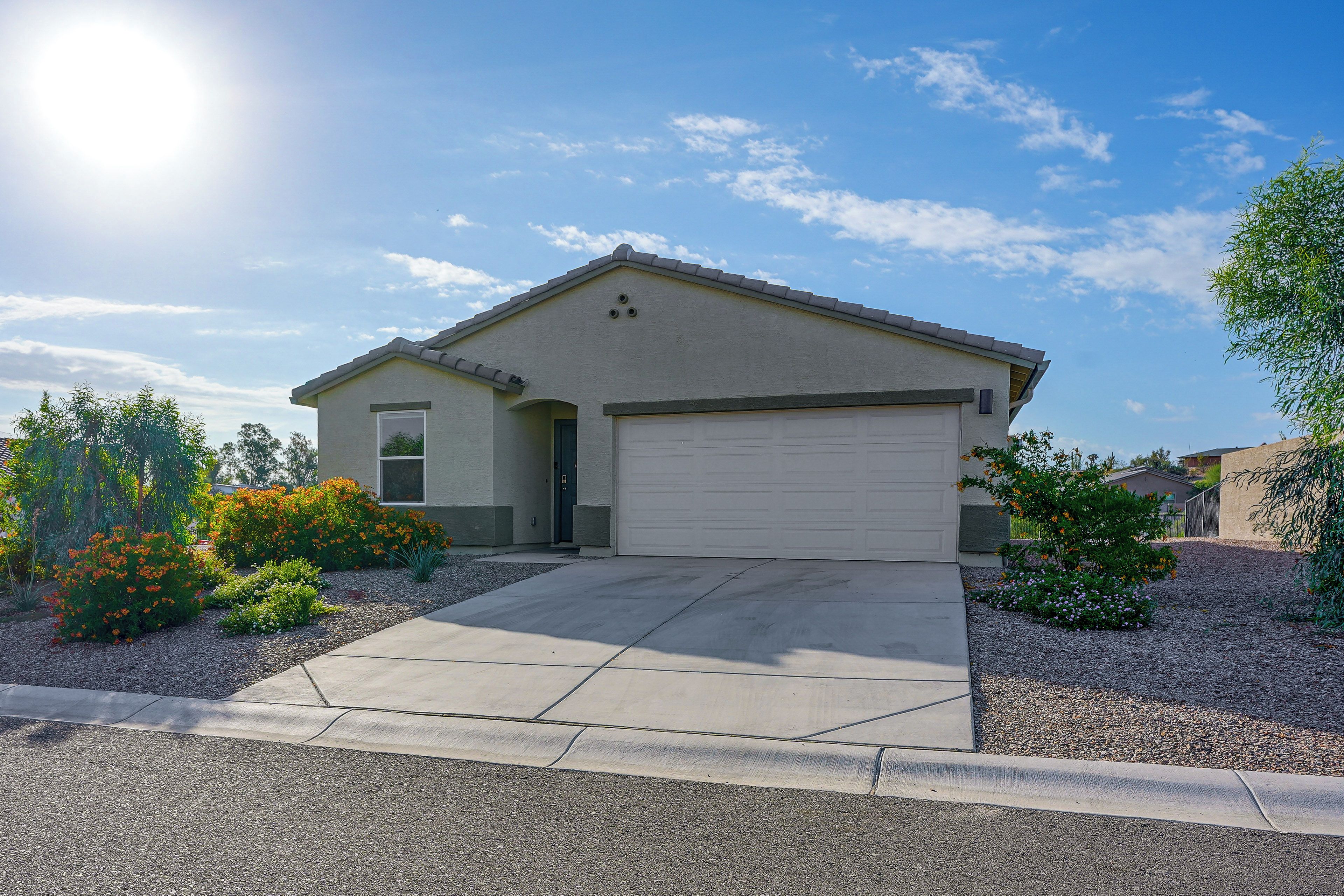 A single-story house with a garage, surrounded by a gravel driveway and landscaped with various shrubs and flowers.