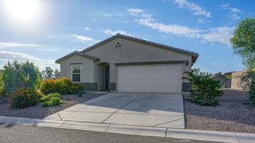 A single-story house with a garage, surrounded by a gravel driveway and landscaped with various shrubs and flowers.