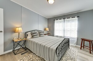 A bedroom with a bed, bedside lamps, a nightstand, a window with curtains, and a wooden stool.