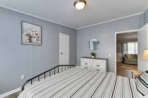 Un dormitorio con cama, cómoda, espejo y una puerta que da a otra habitación.