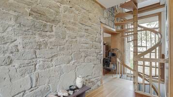 A room with a stone wall, a wooden bench with decorative items, and a spiral staircase leading to an upper level.