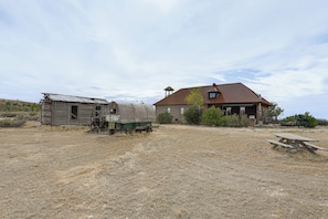 A rustic cabin with a wooden exterior and a metal roof, situated in a dry, grassy field with a clear sky.