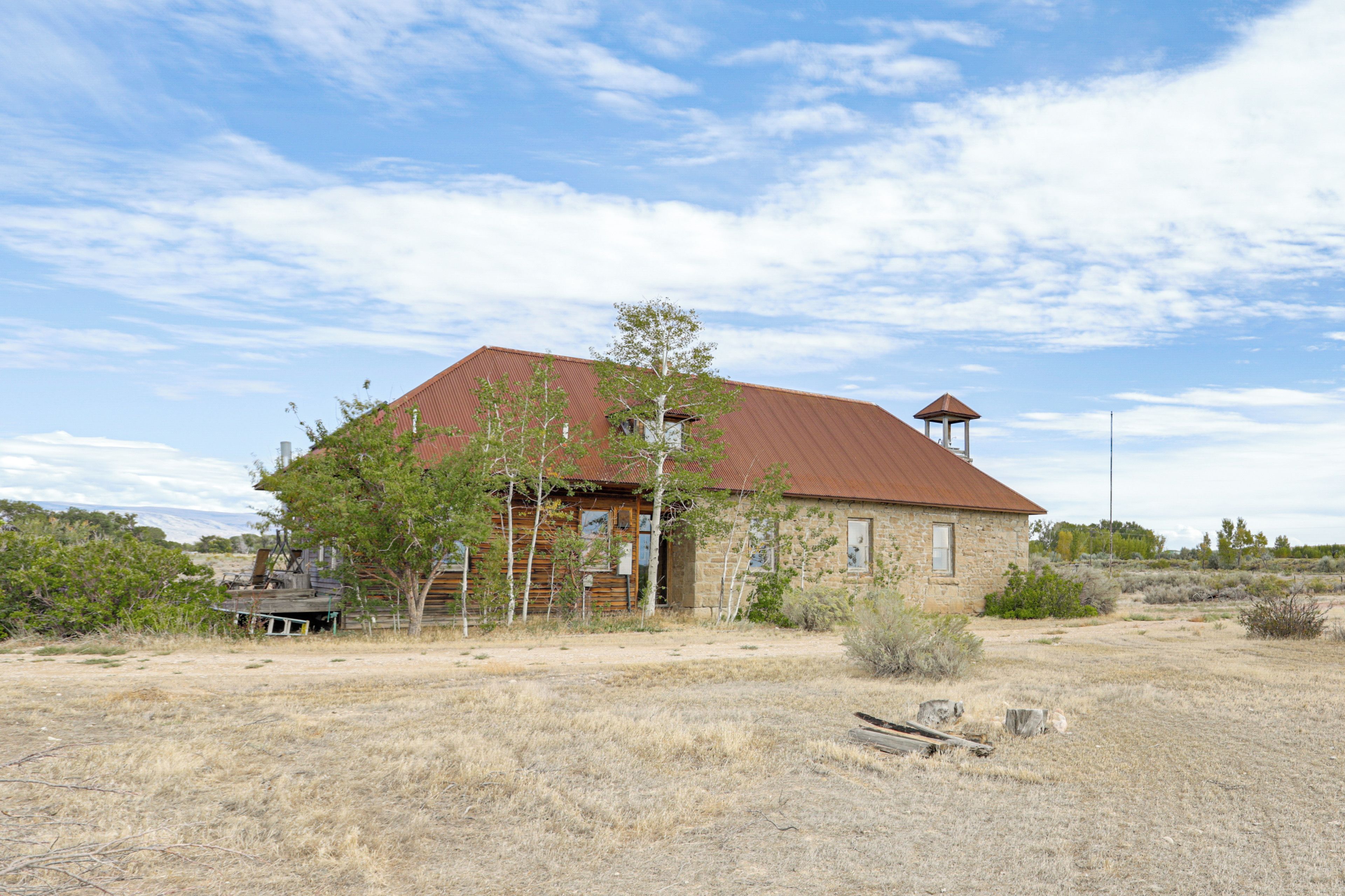A rustic building with a red roof and a small tower, surrounded by dry grass and sparse vegetation.