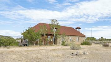 A rustic building with a red roof and a small tower, surrounded by dry grass and sparse vegetation.