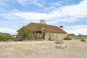 A rustic building with a red roof and a small tower, surrounded by dry grass and sparse vegetation.