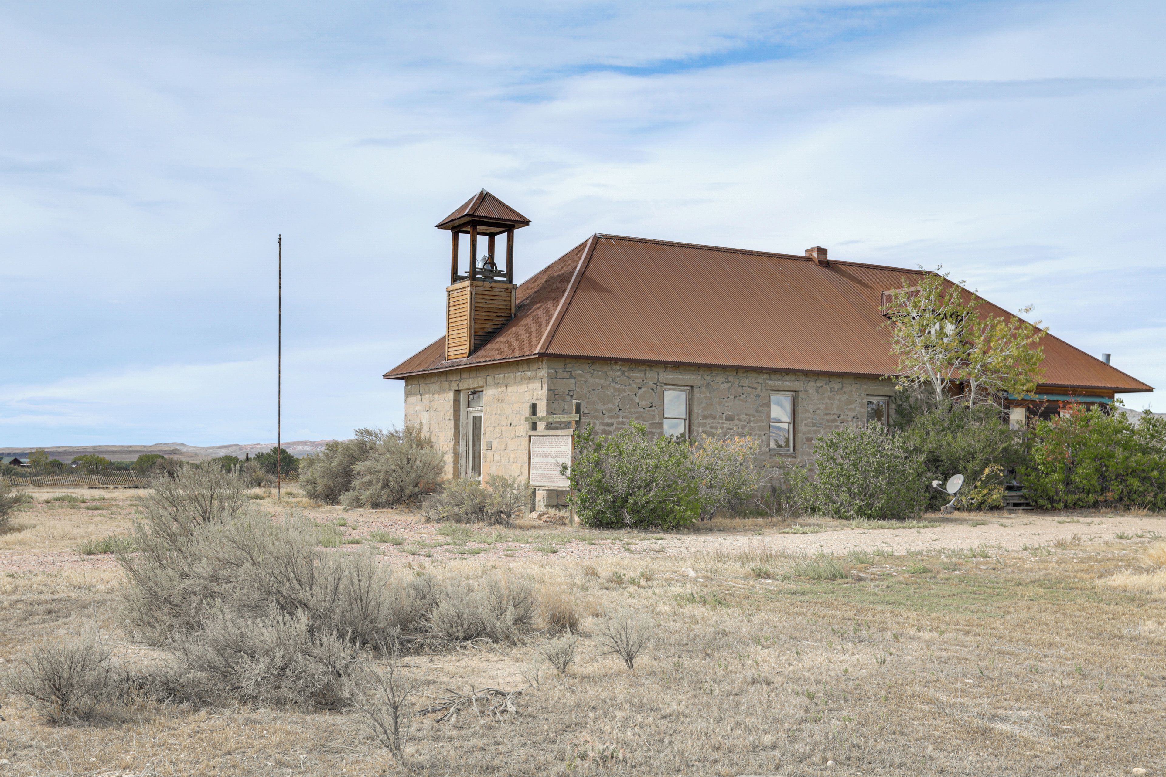 A stone building with a bell tower, surrounded by dry vegetation and a clear sky.