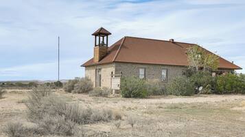 A stone building with a bell tower, surrounded by dry vegetation and a clear sky.
