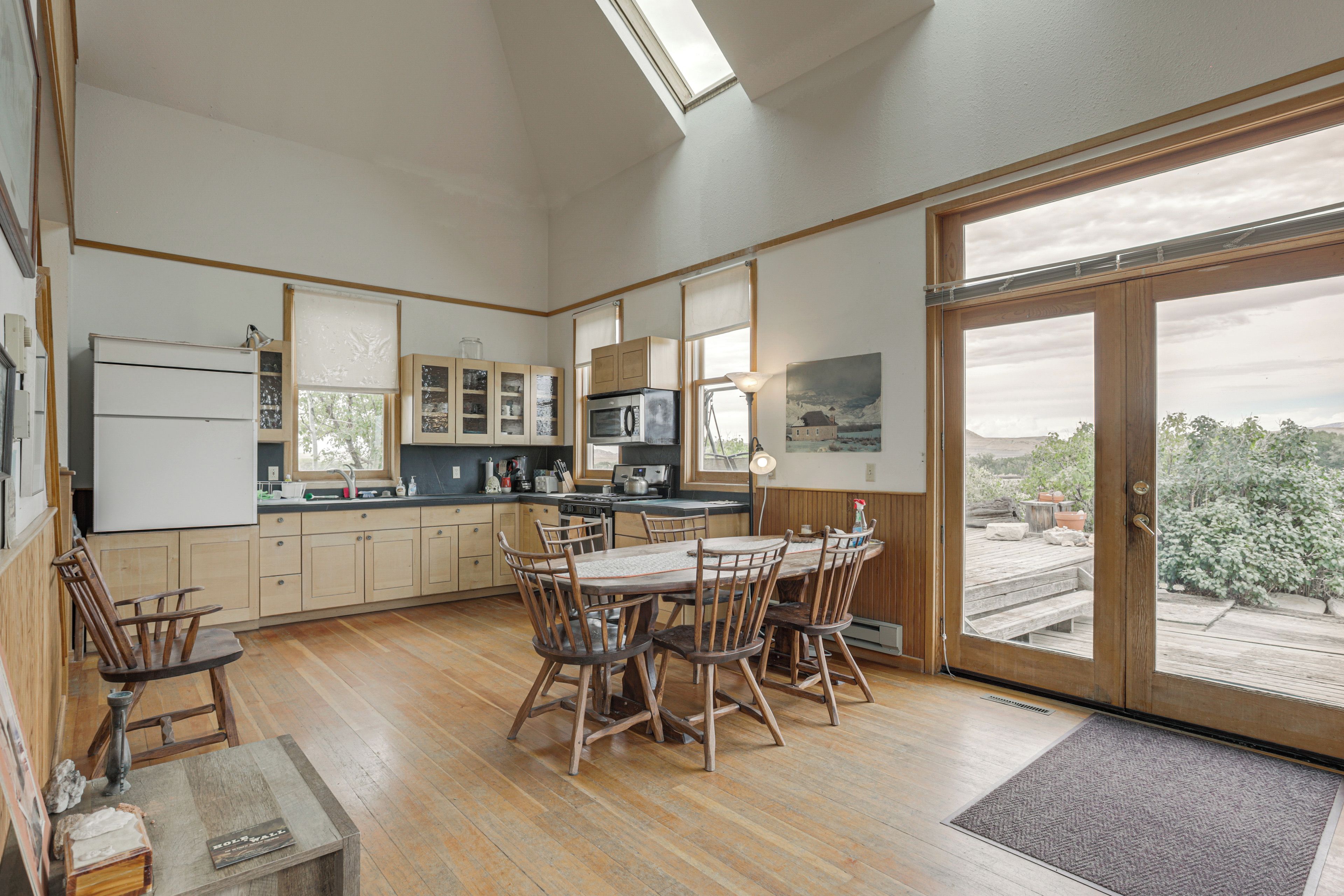 A kitchen with wooden cabinets, a dining table with chairs, a refrigerator, and a large window with a view.