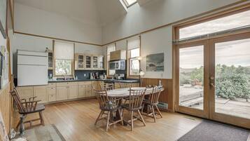 A kitchen with wooden cabinets, a dining table with chairs, a refrigerator, and a large window with a view.