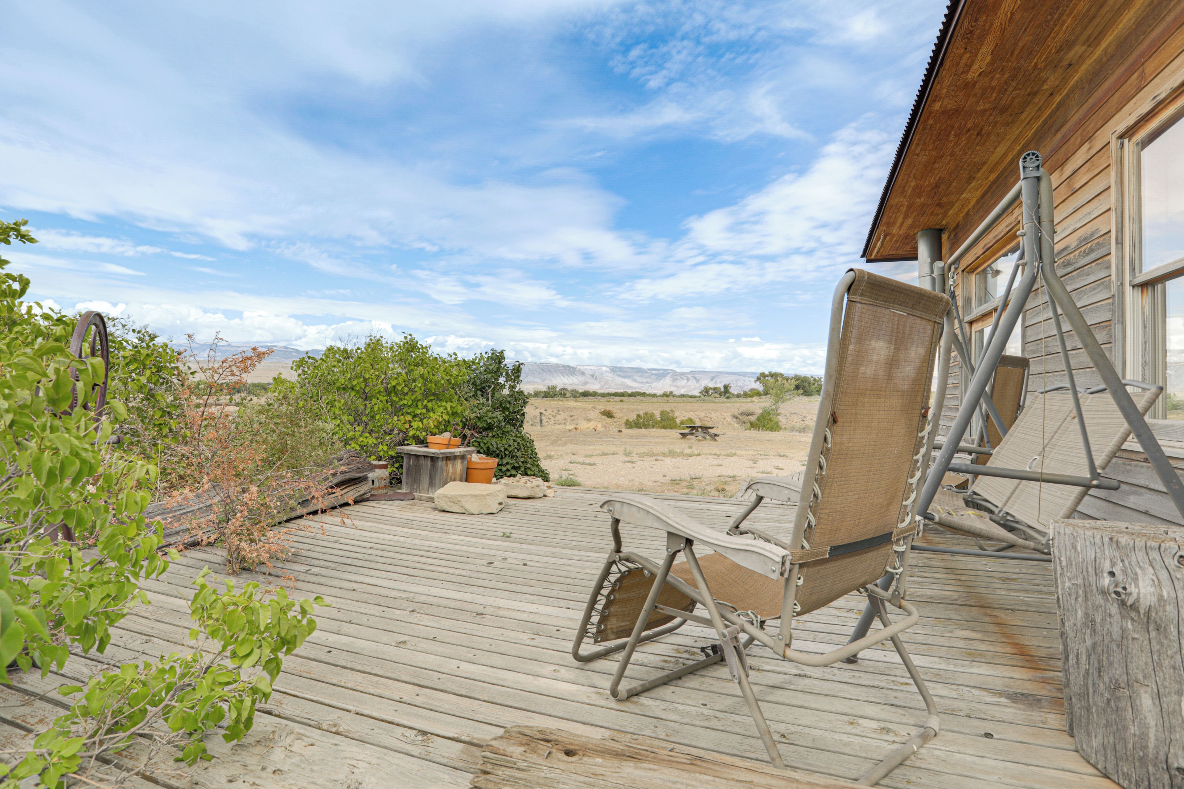 A wooden deck with a metal chair and a table, overlooking a desert landscape with sparse vegetation.