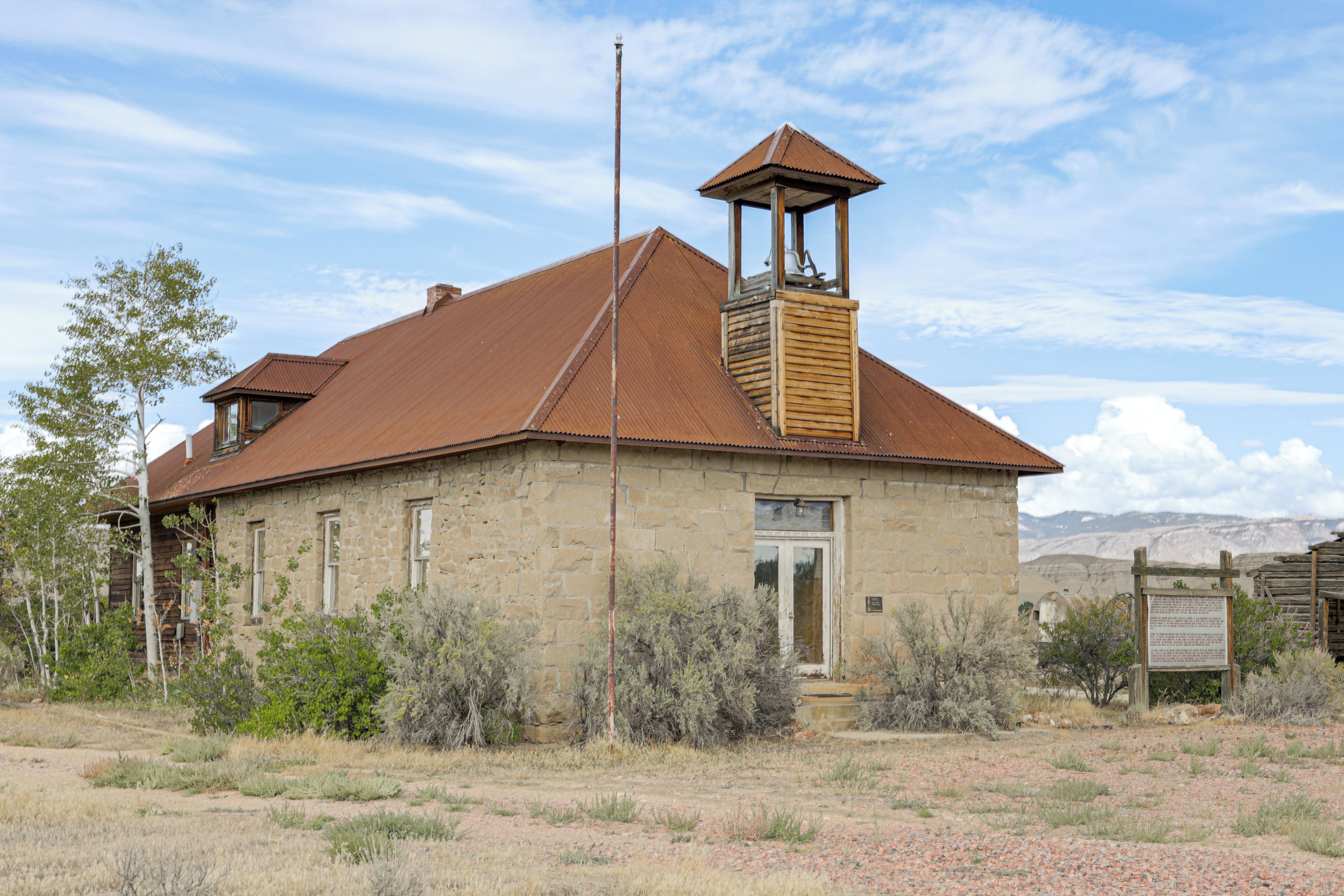A rustic stone building with a metal roof, a wooden bell tower, and a signboard.