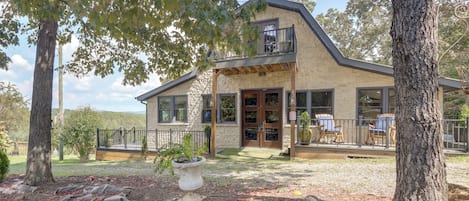 A two-story house with a stone facade, a balcony, and a front porch with outdoor seating.