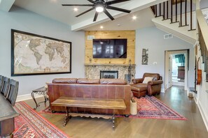 A spacious living room with a large world map, leather sofas, a fireplace, and a staircase leading to another level. - Quiet Countryside Escape w/ Views in Talking Rock (Talking Rock)