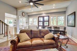 A spacious living room with a brown leather sofa, a dining area with a wooden table and chairs, and large windows allowing natural light.