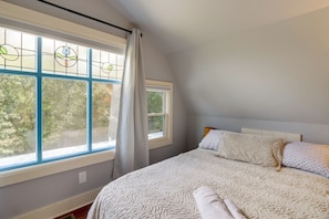 A bedroom with a large window, a bed with white bedding, and a headboard.