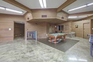 Mesa de bilhar em um salão com paredes de madeira e teto com vigas aparentes.