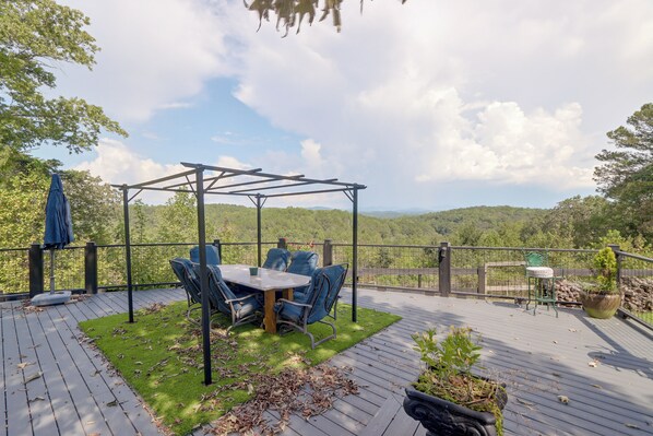 Terraza exterior con pérgola, mobiliario y vistas a un paisaje boscoso.