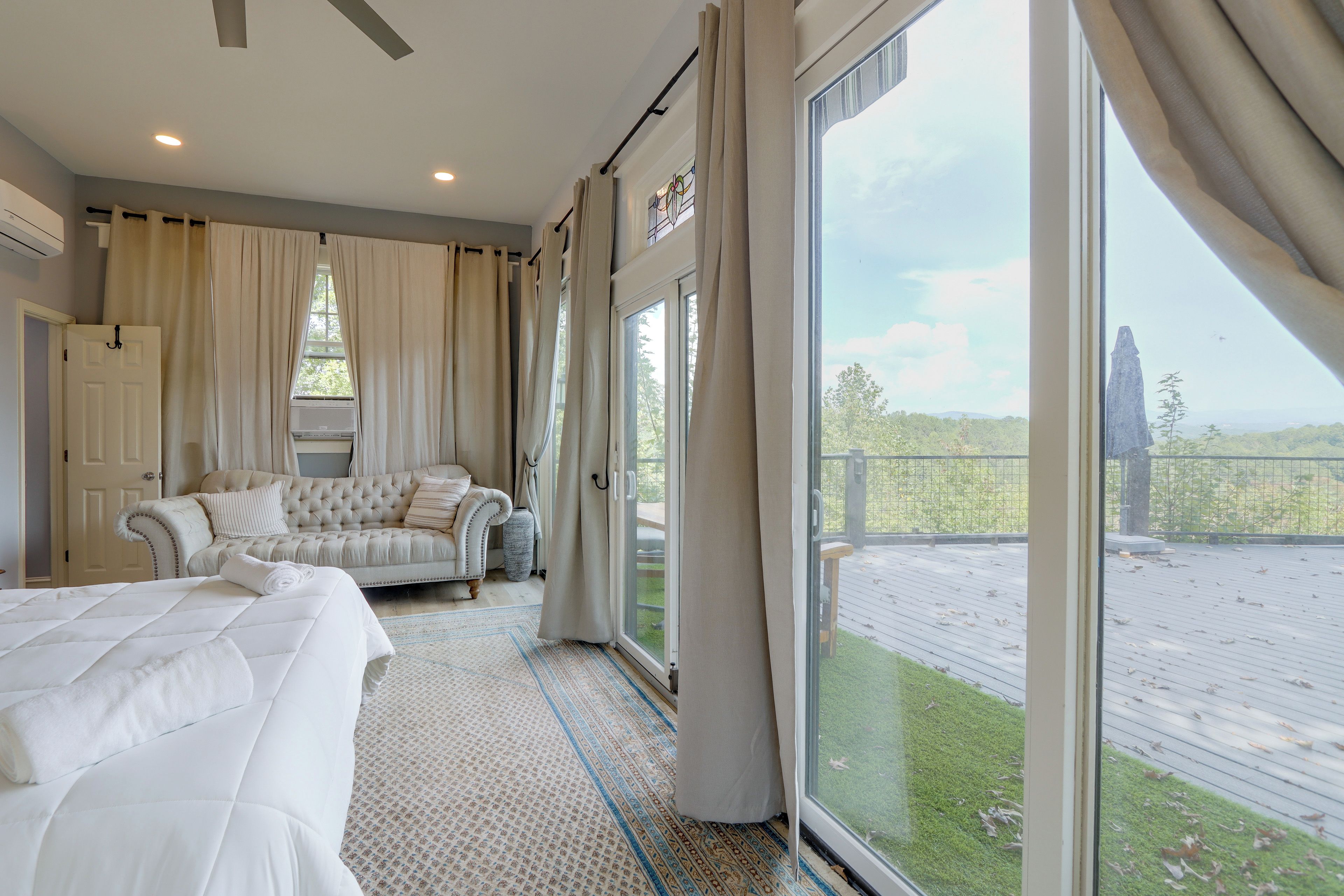 A bedroom with a large bed, a sofa, and a view of a deck.