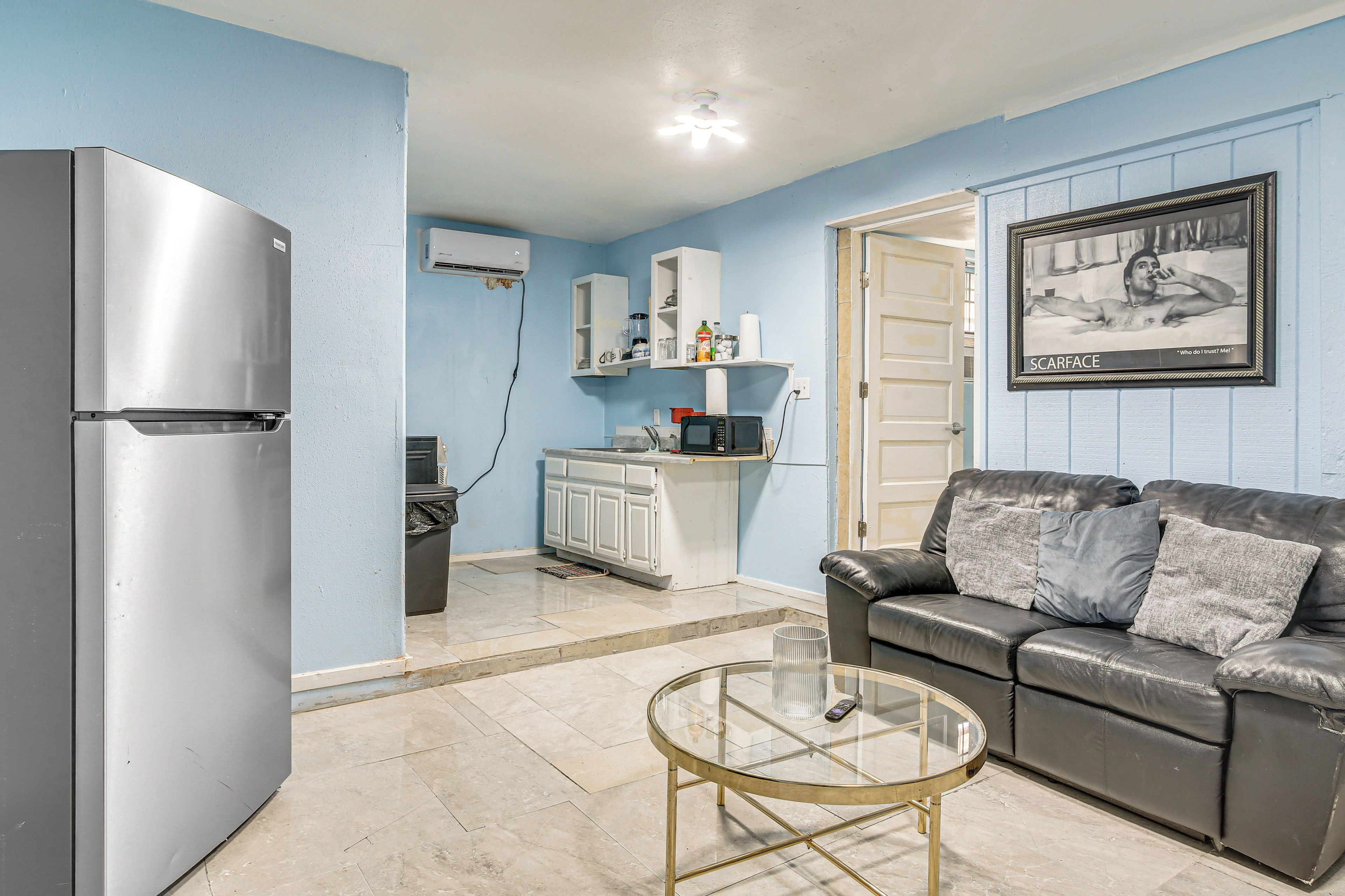 Un espacio habitable compacto con kitchenette, un refrigerador, un microondas, una mesa de centro de vidrio y un sofá de cuero.