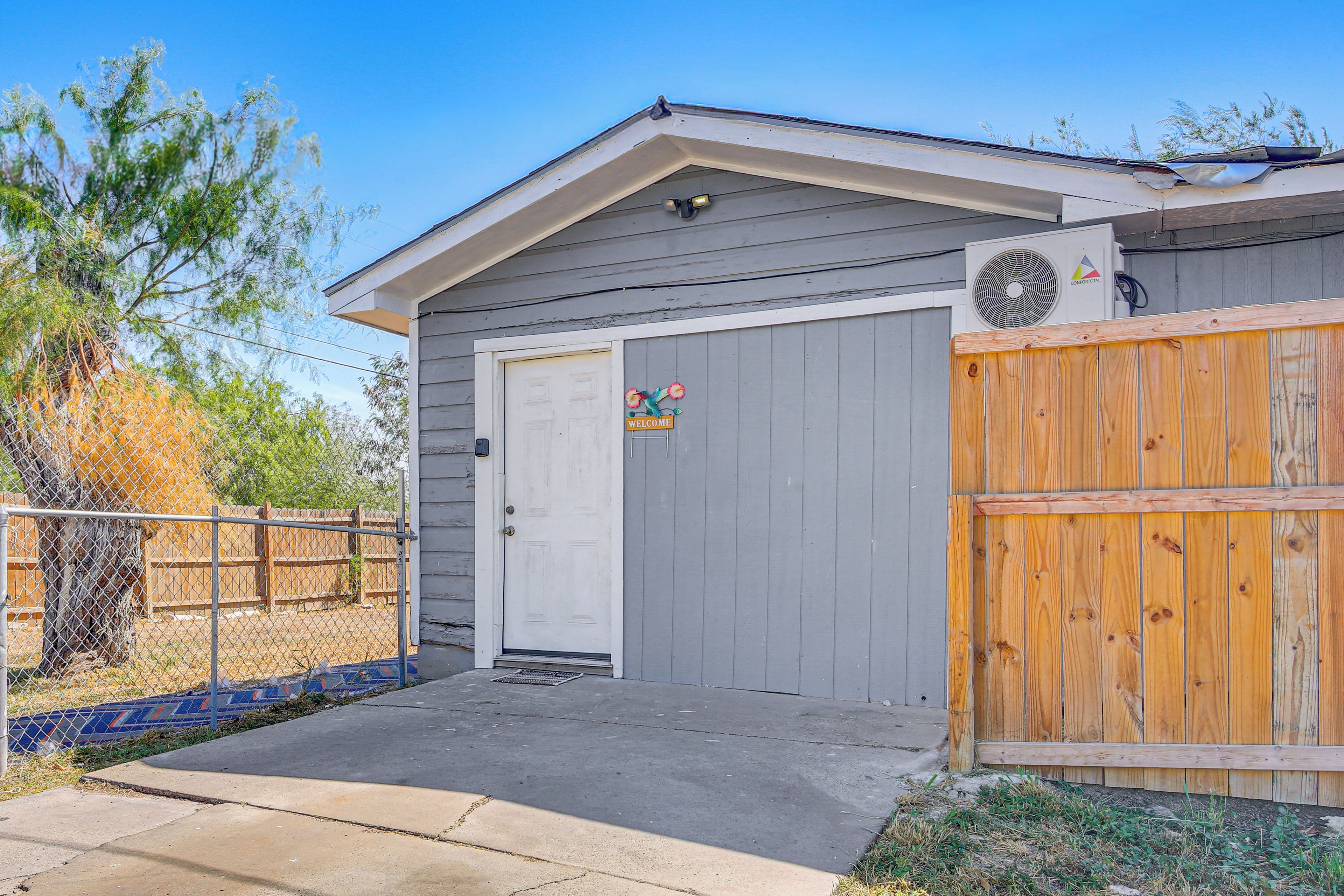 A residential building with a grey exterior, a white door, and a wooden fence.