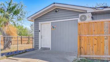 A residential building with a grey exterior, a white door, and a wooden fence.