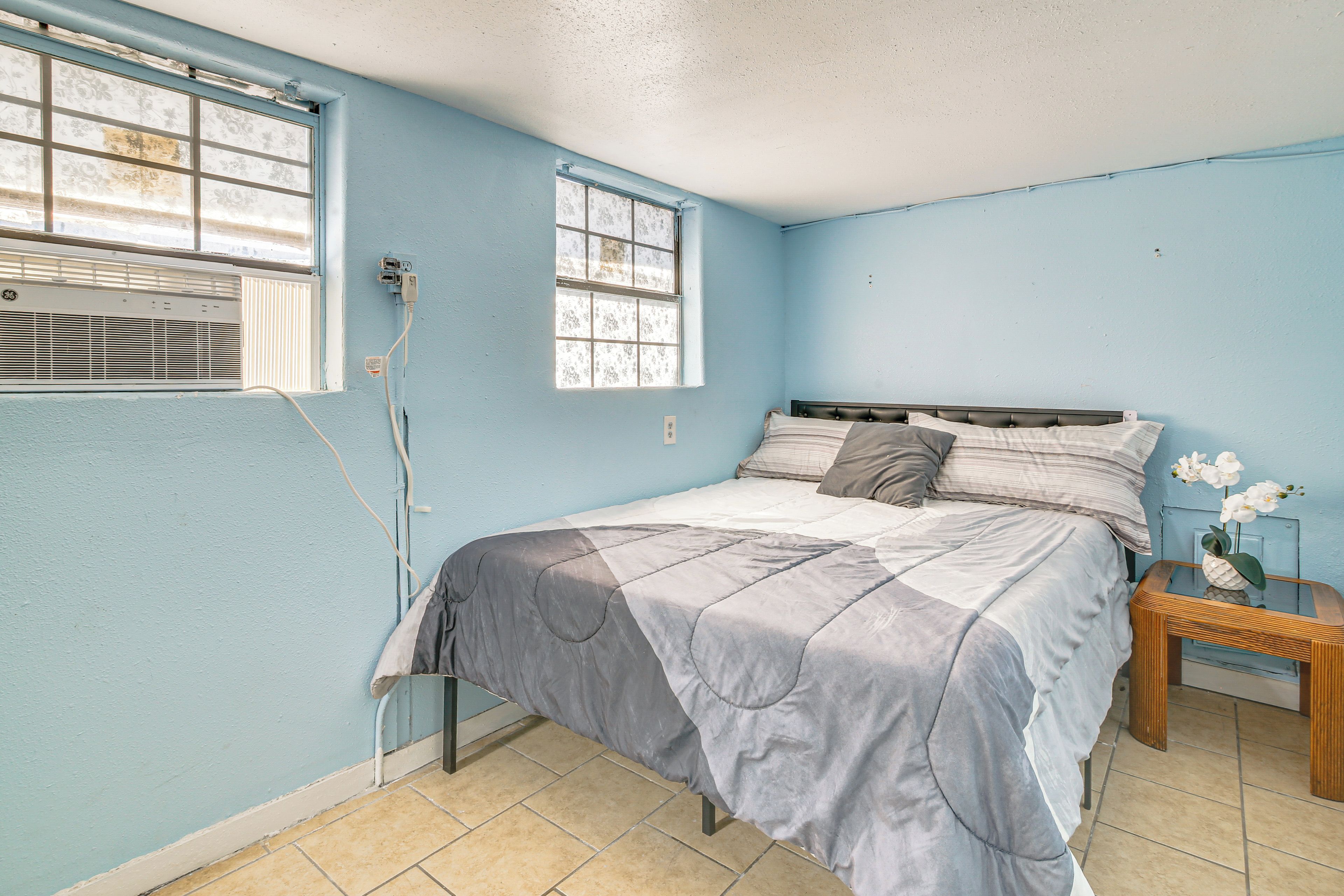 A bedroom with a bed, a nightstand, a window, and an air conditioning unit.