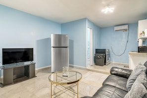 A living room with a flat-screen TV, a stainless steel refrigerator, a glass coffee table, a leather sofa, and a kitchen area with a microwave and a trash bin. - Gateway to Downtown Harlingen! Quaint Unit (Harlingen)