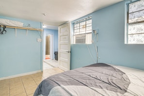 A bedroom with a bed, a window with a view, a door, and a wall-mounted air conditioning unit. - Gateway to Downtown Harlingen! Quaint Unit (Harlingen)
